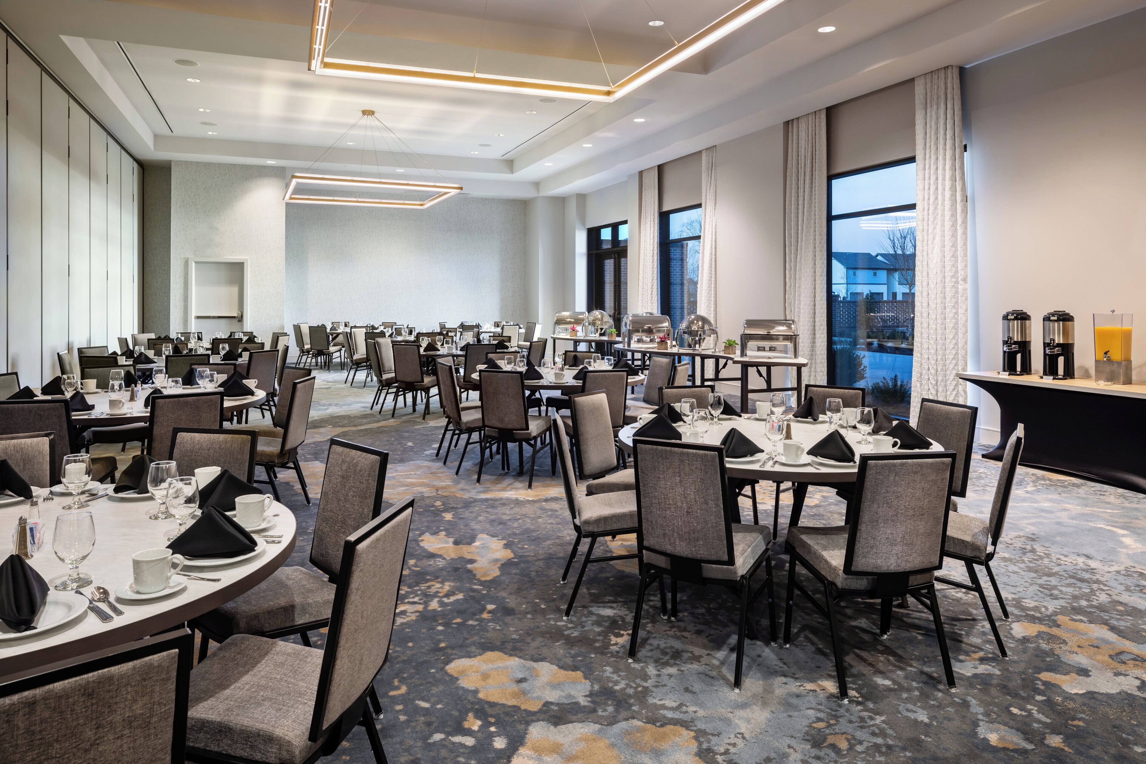 A hotel dining area with multiple tables and chairs, equipped with glassware and napkins.