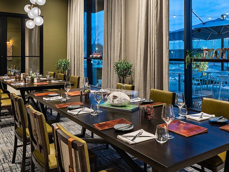 A dining area with a long table set for a meal, chairs, and a view of outdoor seating.