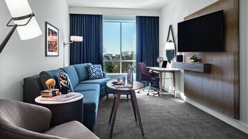 Una habitación de hotel moderna con sofá, sillón, mesa de comedor y televisor de pantalla plana montado en la pared.