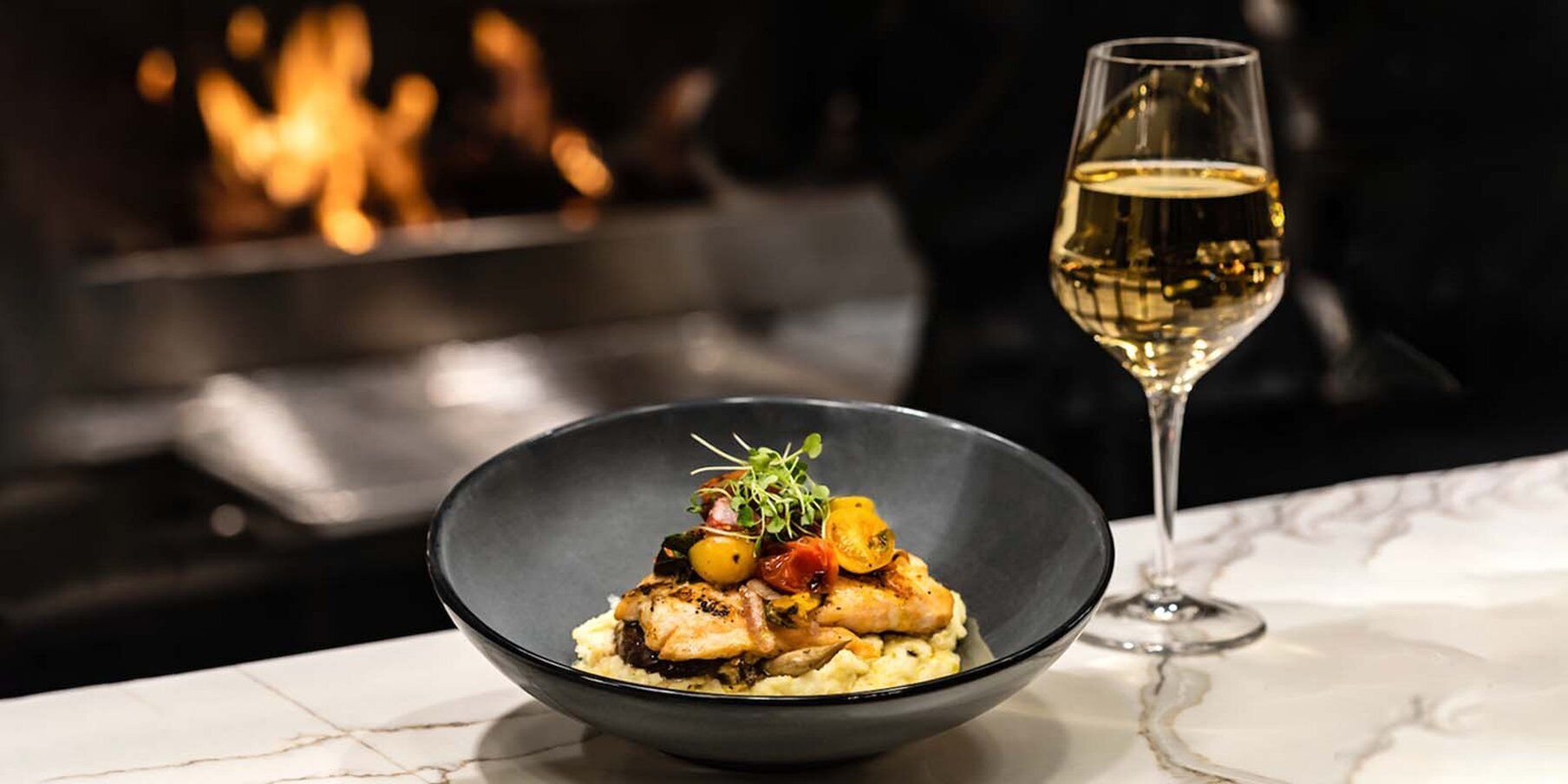 Un plato de comida con una copa de vino blanco sobre una mesa de mármol.
