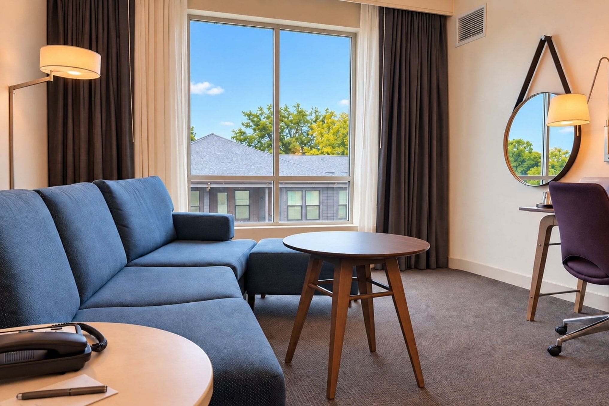 Habitación de hotel con sofá, una mesita redonda, una silla, lámpara y espejo.
