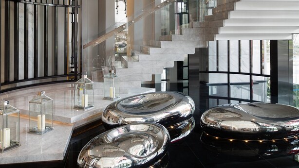 Um interior moderno com uma escadaria curva, superfícies refletoras e luminárias contemporâneas.