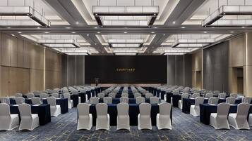 A conference room with rows of tables and chairs, a podium, and a large screen displaying 'COURTYARD BY MARIEOTTA'.
