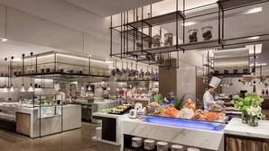 Disposição moderna de buffet com diversas estações de comida, um chef preparando alimentos e ambiente limpo e bem iluminado.