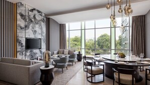 Uma sala de estar moderna com uma televisão grande, assentos confortáveis, uma área de jantar com uma mesa redonda e grandes janelas com vista para o exterior.