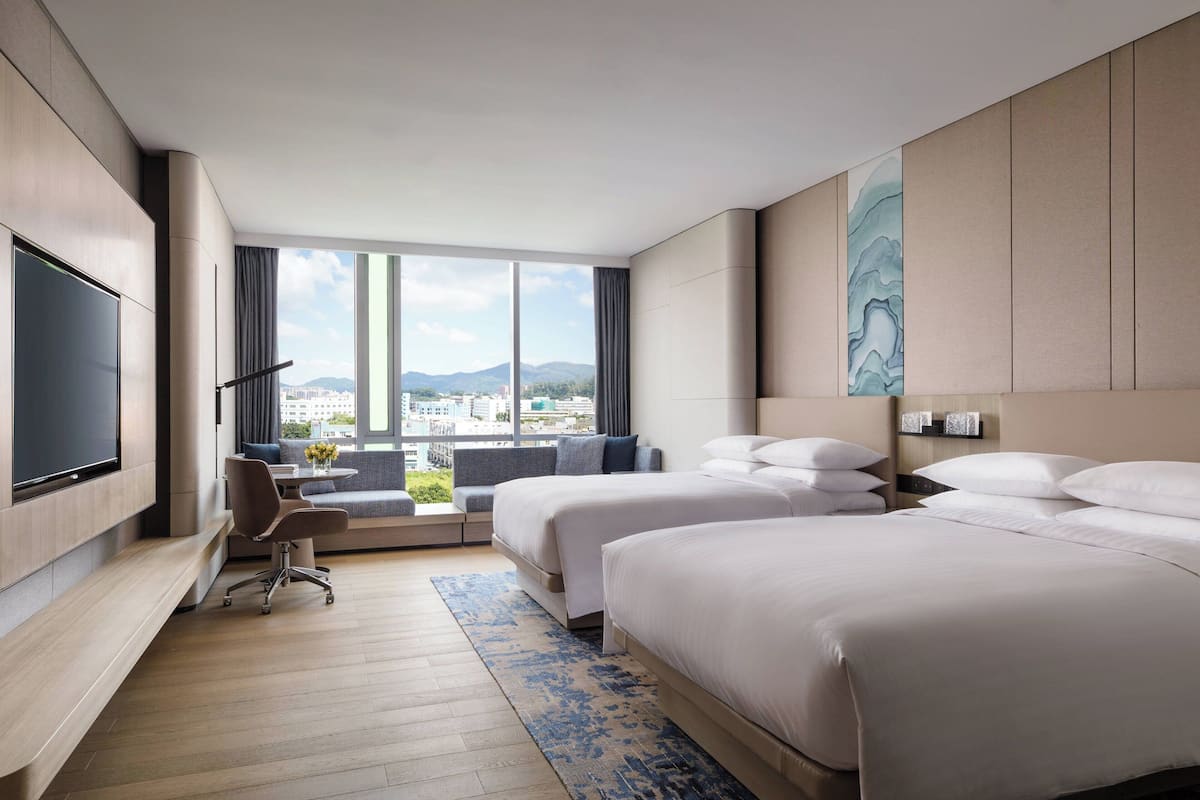Hotelkamer met twee bedden, een bureau, een stoel, een televisie en een groot raam met uitzicht op de stad.