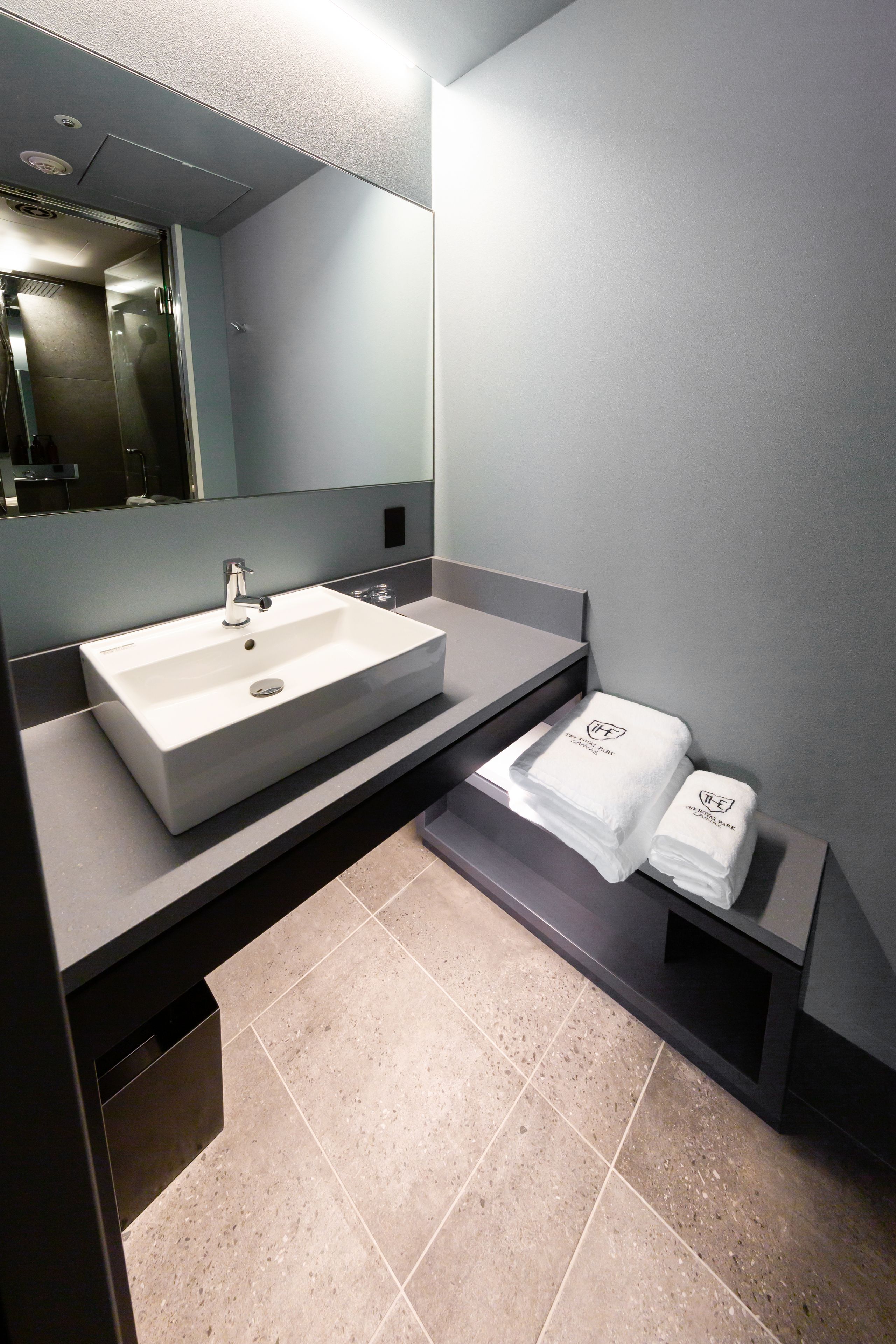 A modern bathroom with a large sink, a mirror, and two towels on a shelf.
