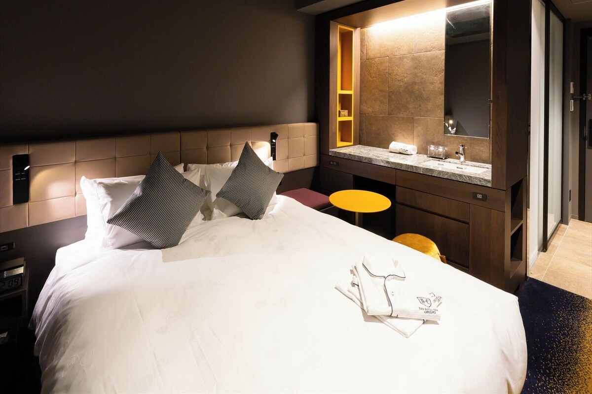 Hotelkamer met een bed, nachtkastje, klein rond tafeltje, spiegel en een badkamer met wastafel en spiegel.