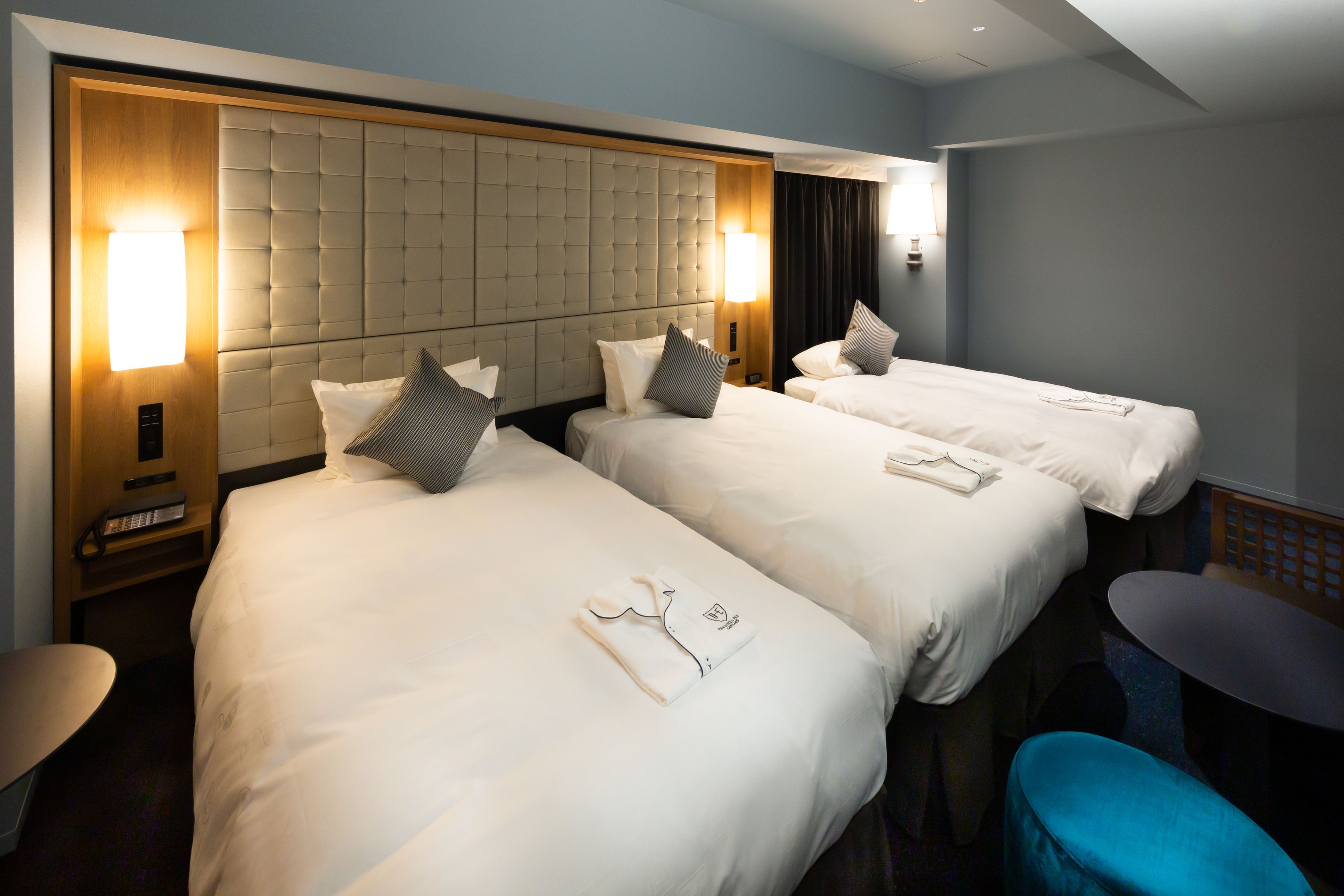A hotel room with three beds, a small table, and a blue chair.