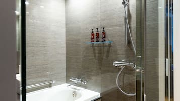 A modern bathroom with a glass-enclosed shower, a white bathtub, and a shelf with toiletries.