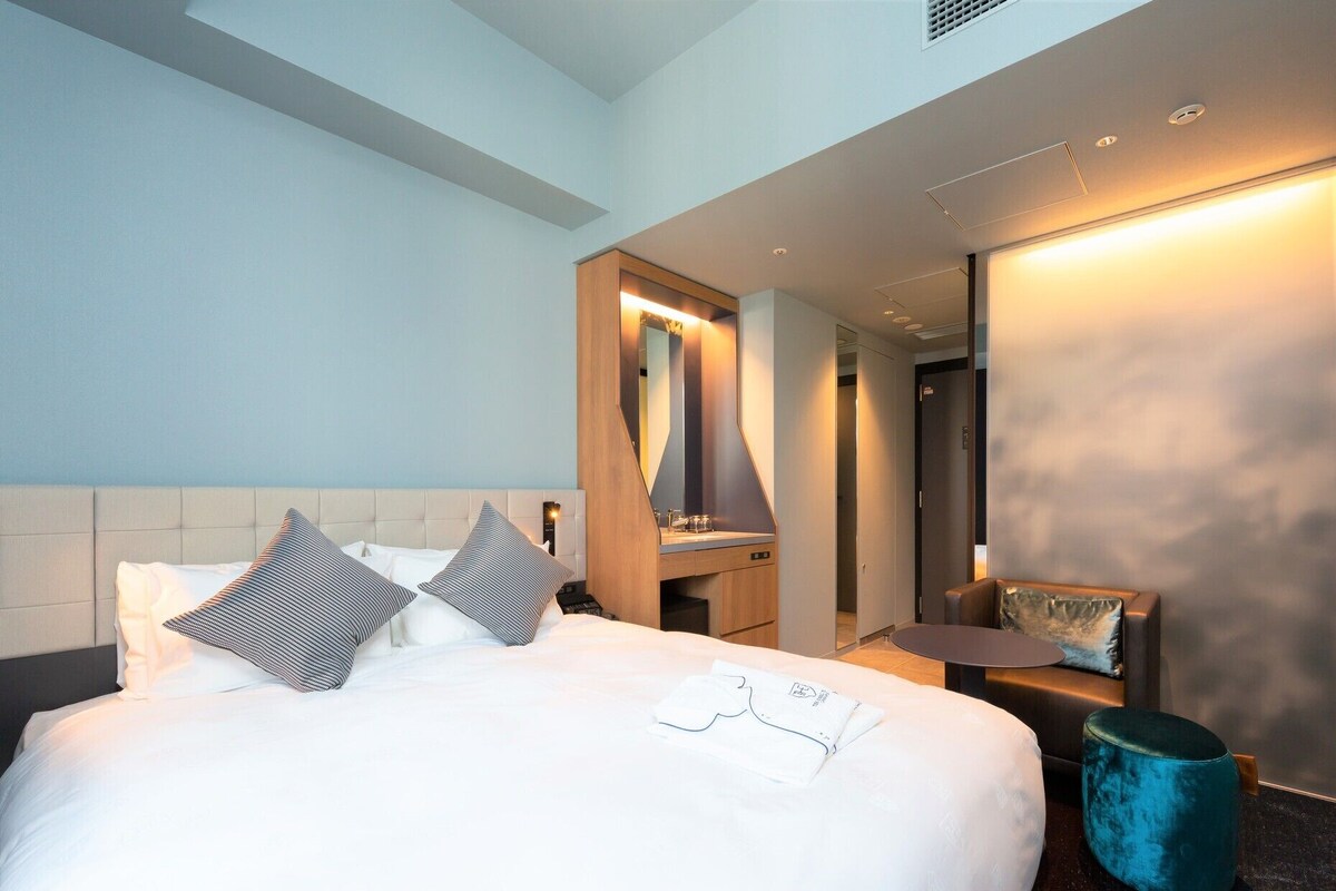 Een hotelkamer met een bed, nachtkastje, spiegel en een zithoekje.