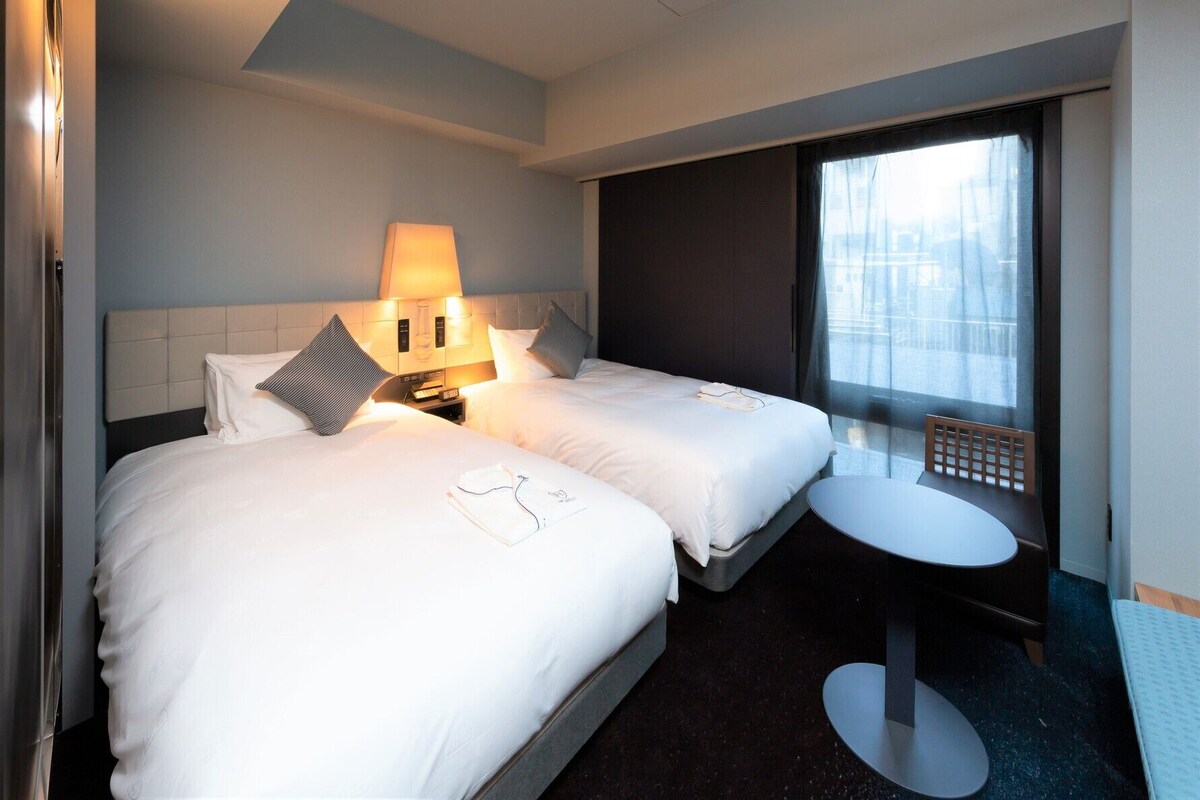 Een hotelkamer met twee bedden, een nachtkastje, een raam met uitzicht en een plafondlamp.