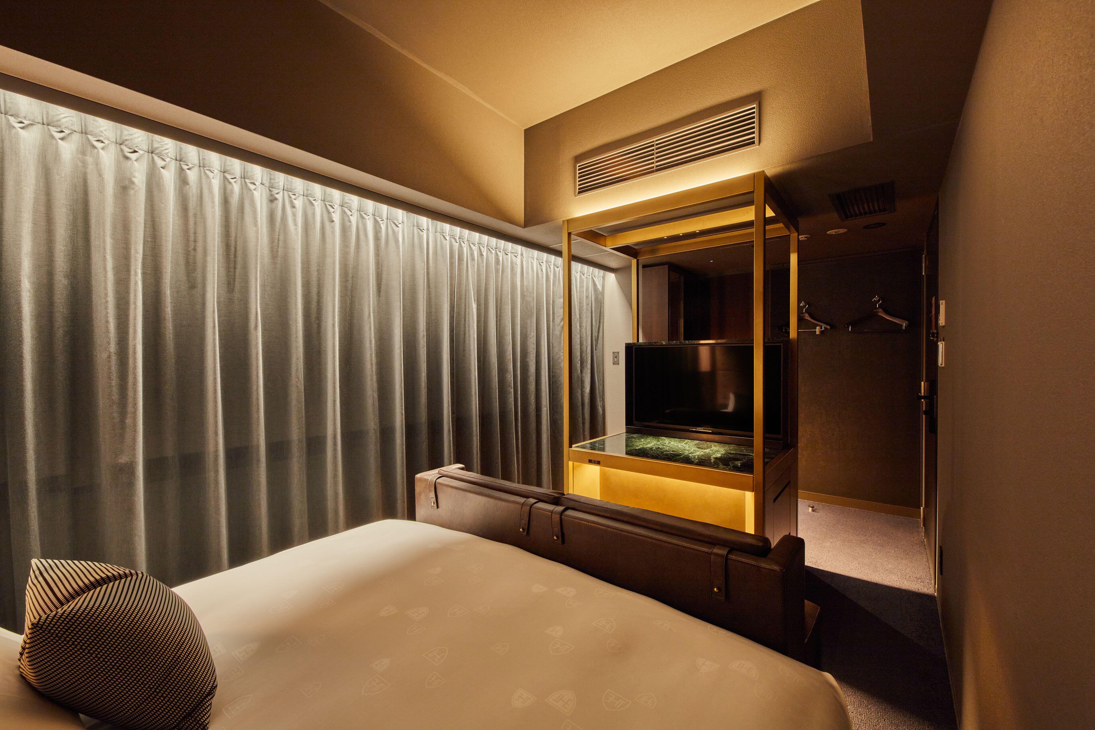 A hotel room with a bed, a TV, a mirror, and a window with curtains.
