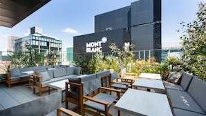 Un espace extérieur aménagé avec des meubles modernes, un grand bâtiment portant l’inscription « MONT BLANC », et une vue sur la ville en arrière-plan.
