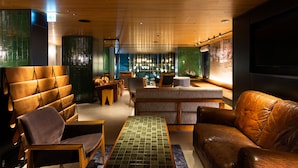 Un espace de détente moderne avec des canapés en cuir, des tables en bois et un bar agrémenté de luminaires suspendus.