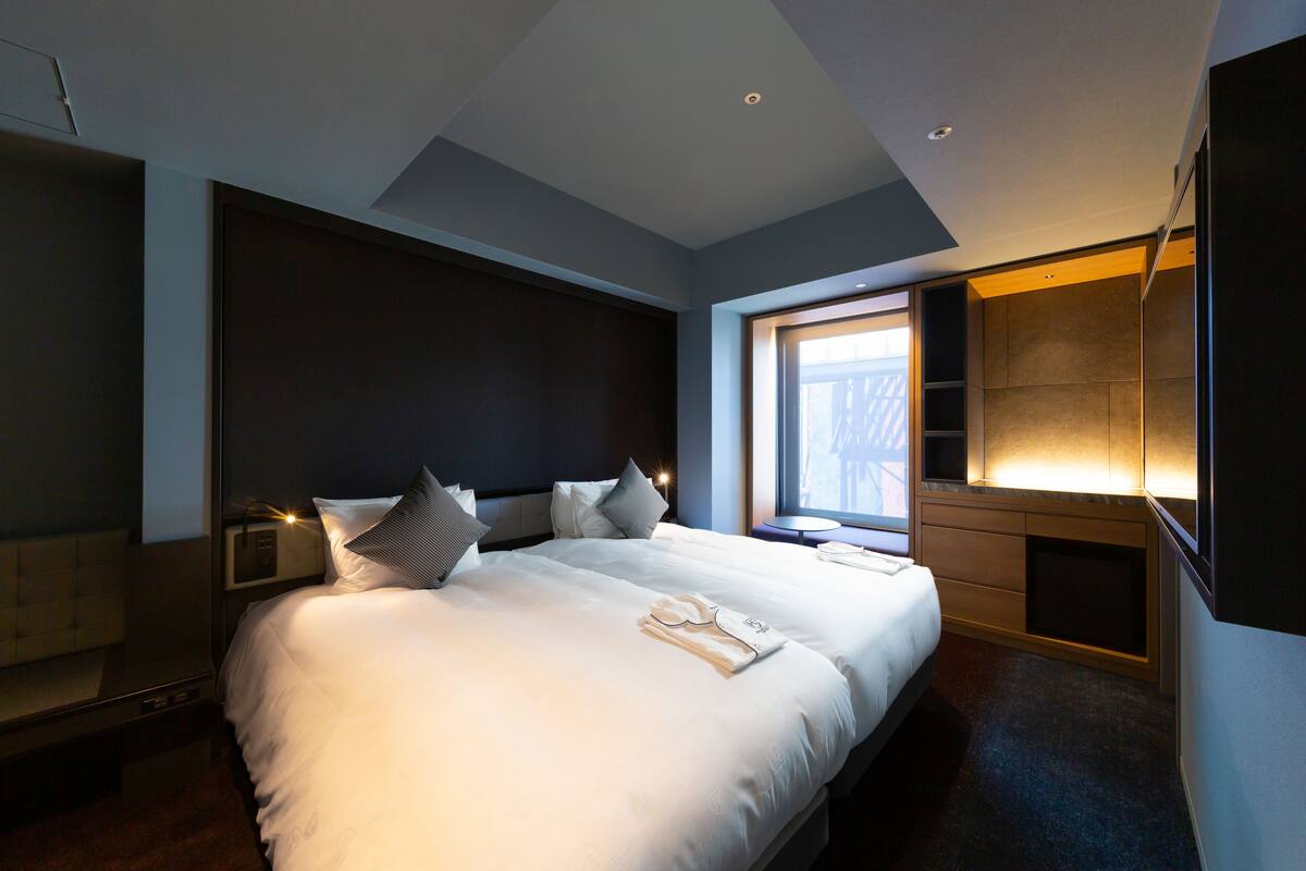 Moderni hotellihuone, jossa on suuri sänky, yöpöydät, televisio ja ikkuna, josta tulee luonnonvaloa.