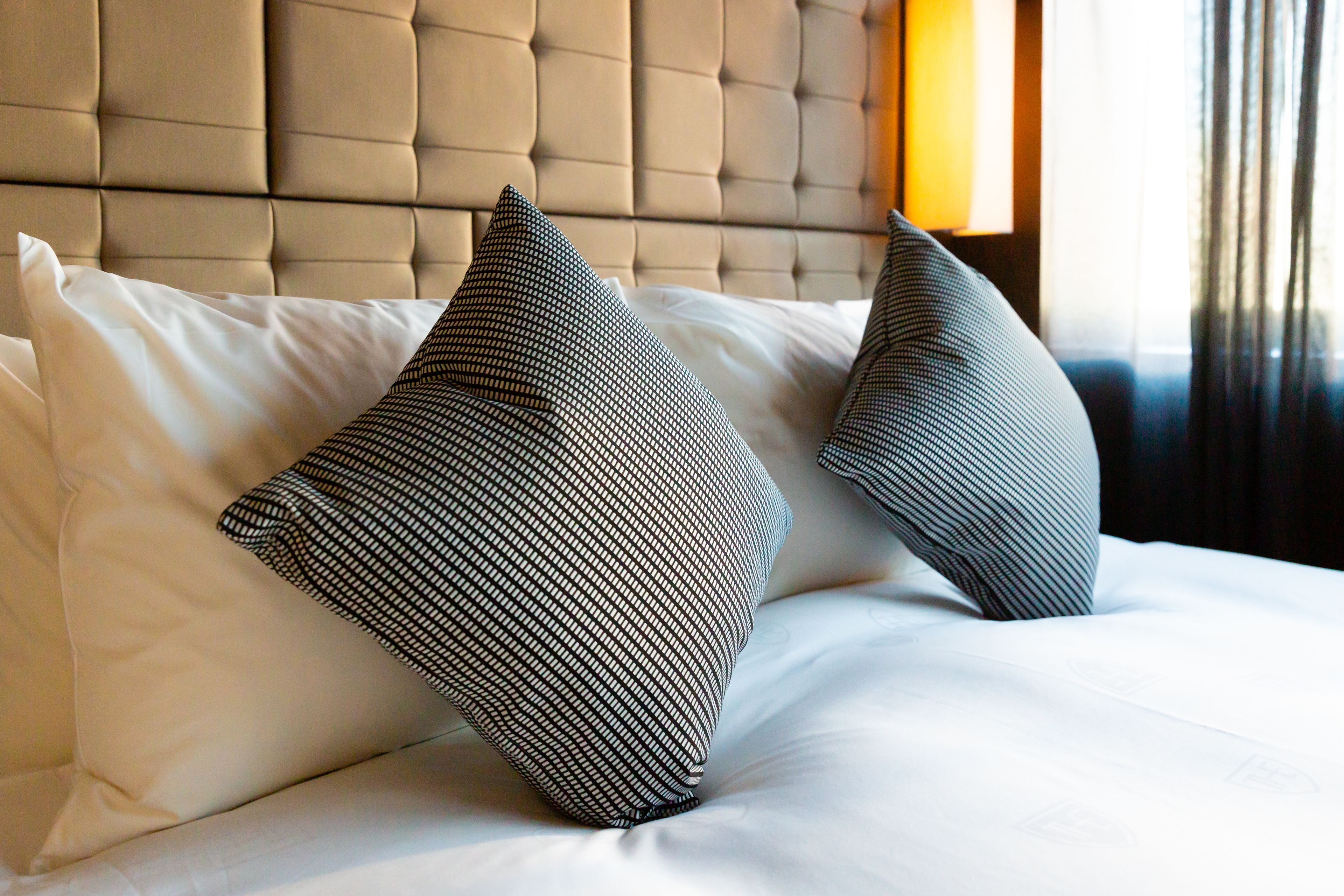 Una cama con cabecera capitonada y dos almohadas estampadas.