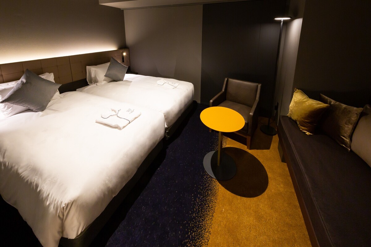 Een hotelkamer met een bed, een klein rond tafeltje, een stoel en een bank.