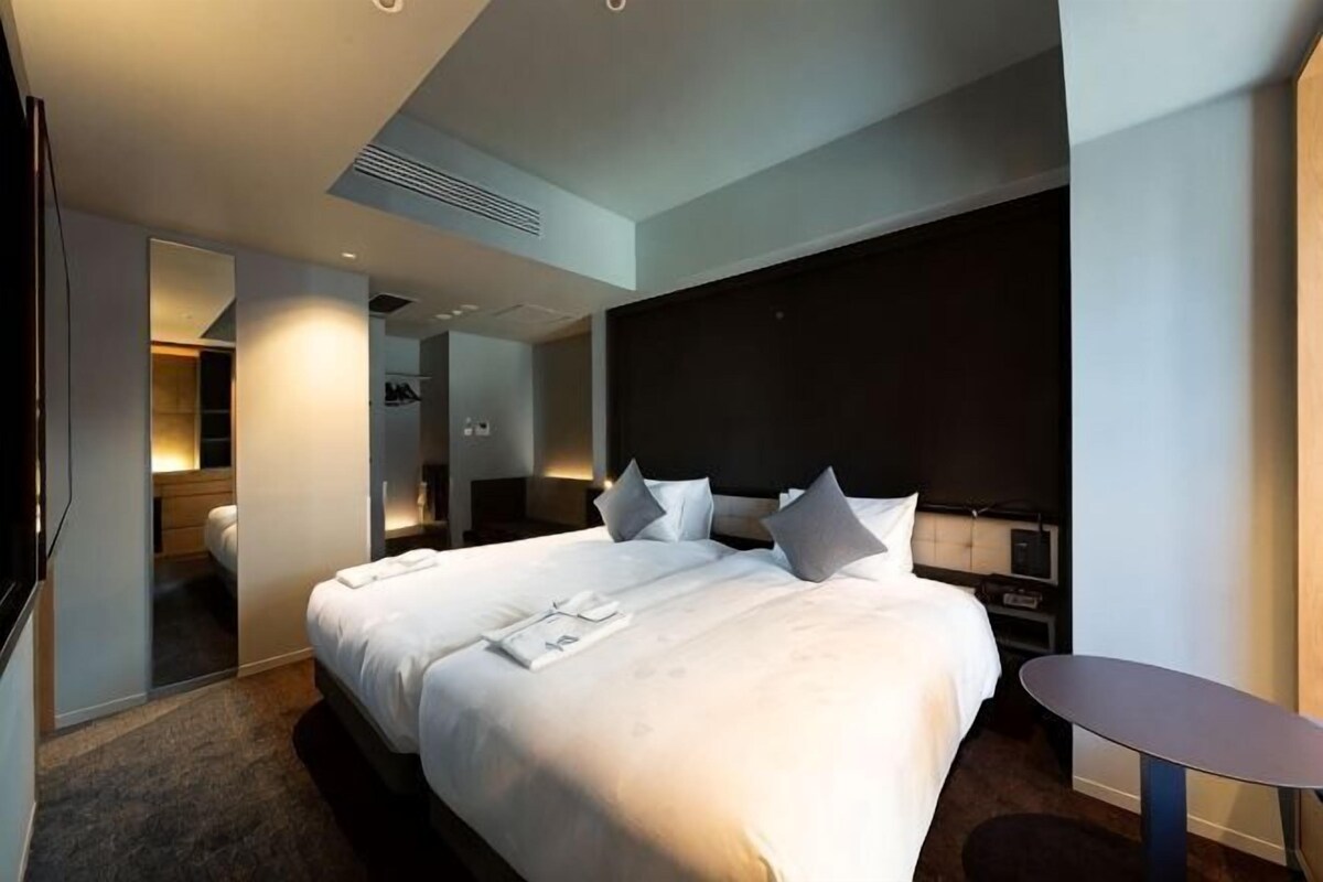 Een moderne hotelkamer met een groot bed, nachtkastjes, een klein tafeltje en een inloopkast.