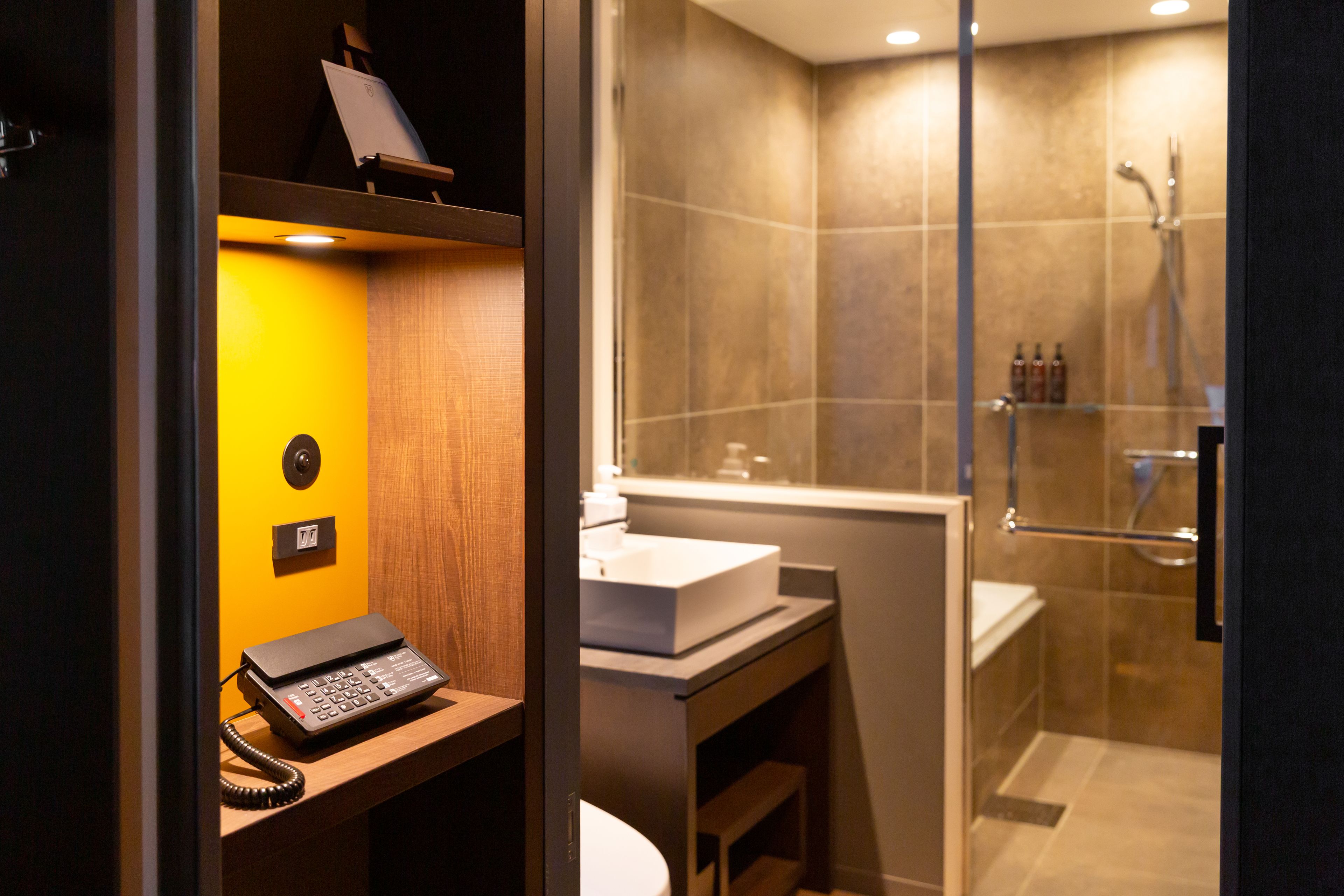 A modern bathroom with a glass-enclosed shower, a wooden vanity with a sink, and a telephone on a shelf.