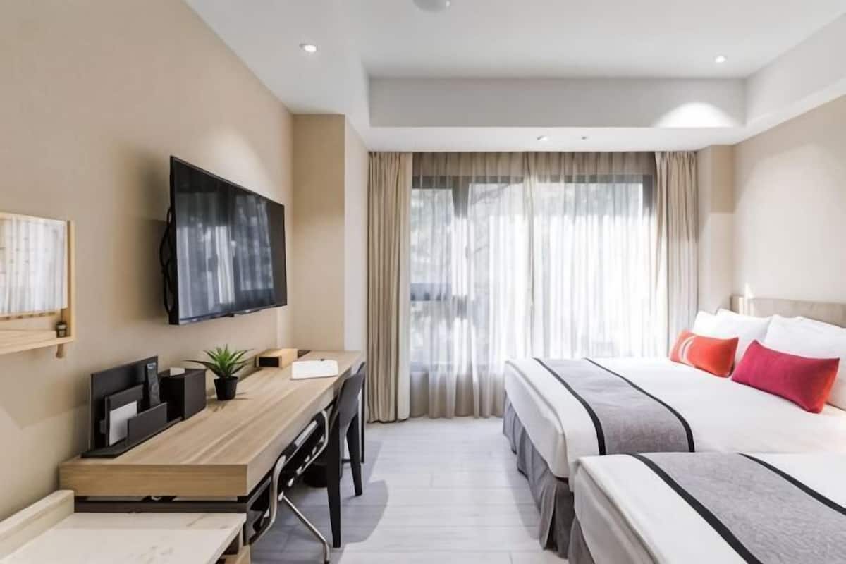 A hotel room with a bed, a desk with a TV, a window with curtains, and a view of the outside.
