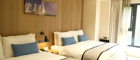 Habitación de hotel con dos camas, una mesita de noche, una lámpara, un cuadro y una ventana con cortinas.