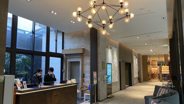 A modern hotel lobby with a reception desk, large windows, a chandelier, and seating area. - Icasa By GoGo Hotel (Taichung)