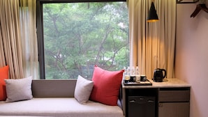 A room with a sofa, pillows, a small table with a coffee maker, bottles, and a view of trees through a window. - Icasa By GoGo Hotel (Taichung)