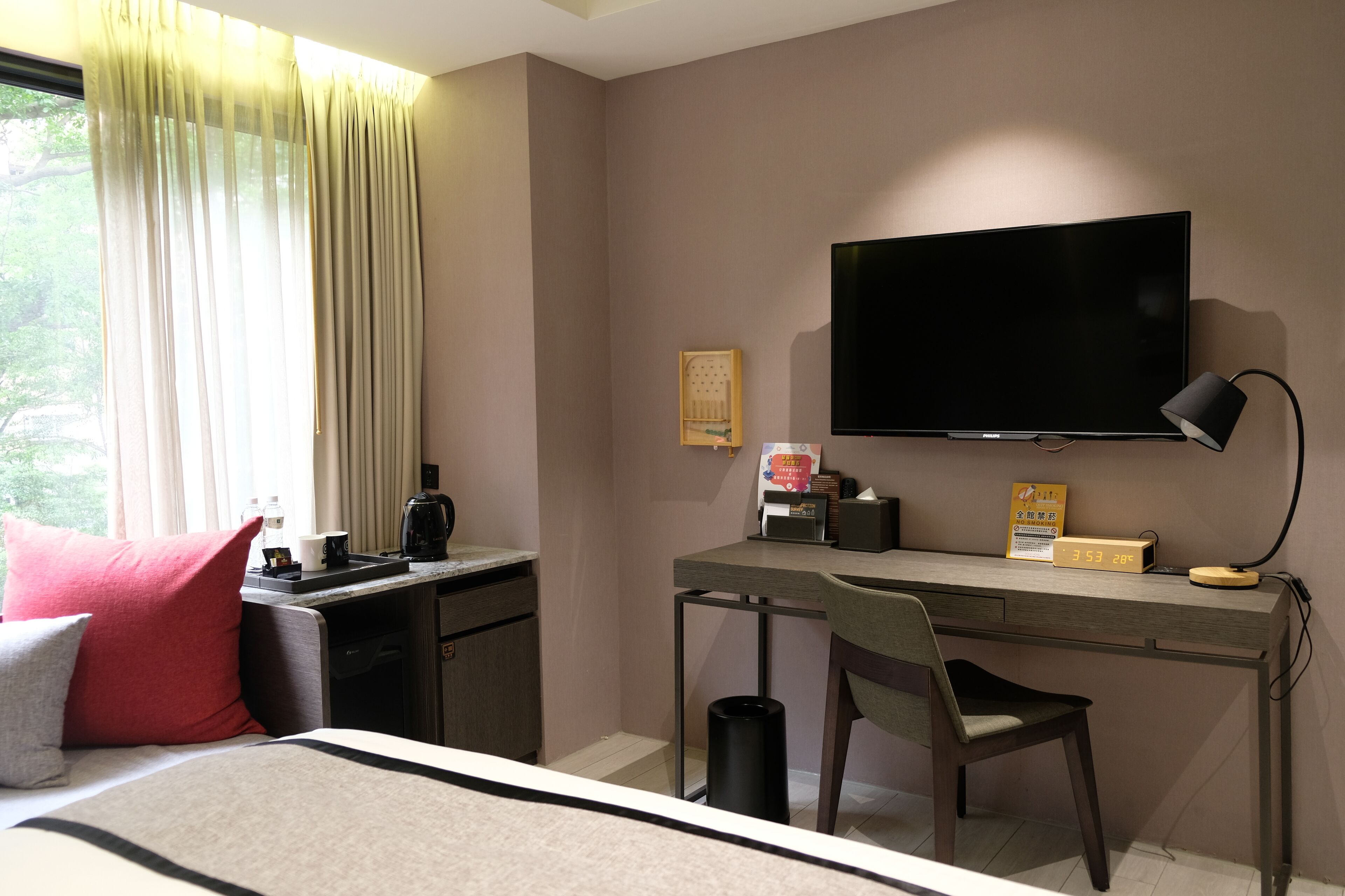 A hotel room with a bed, a desk, a chair, a TV, a lamp, and a window with curtains.
