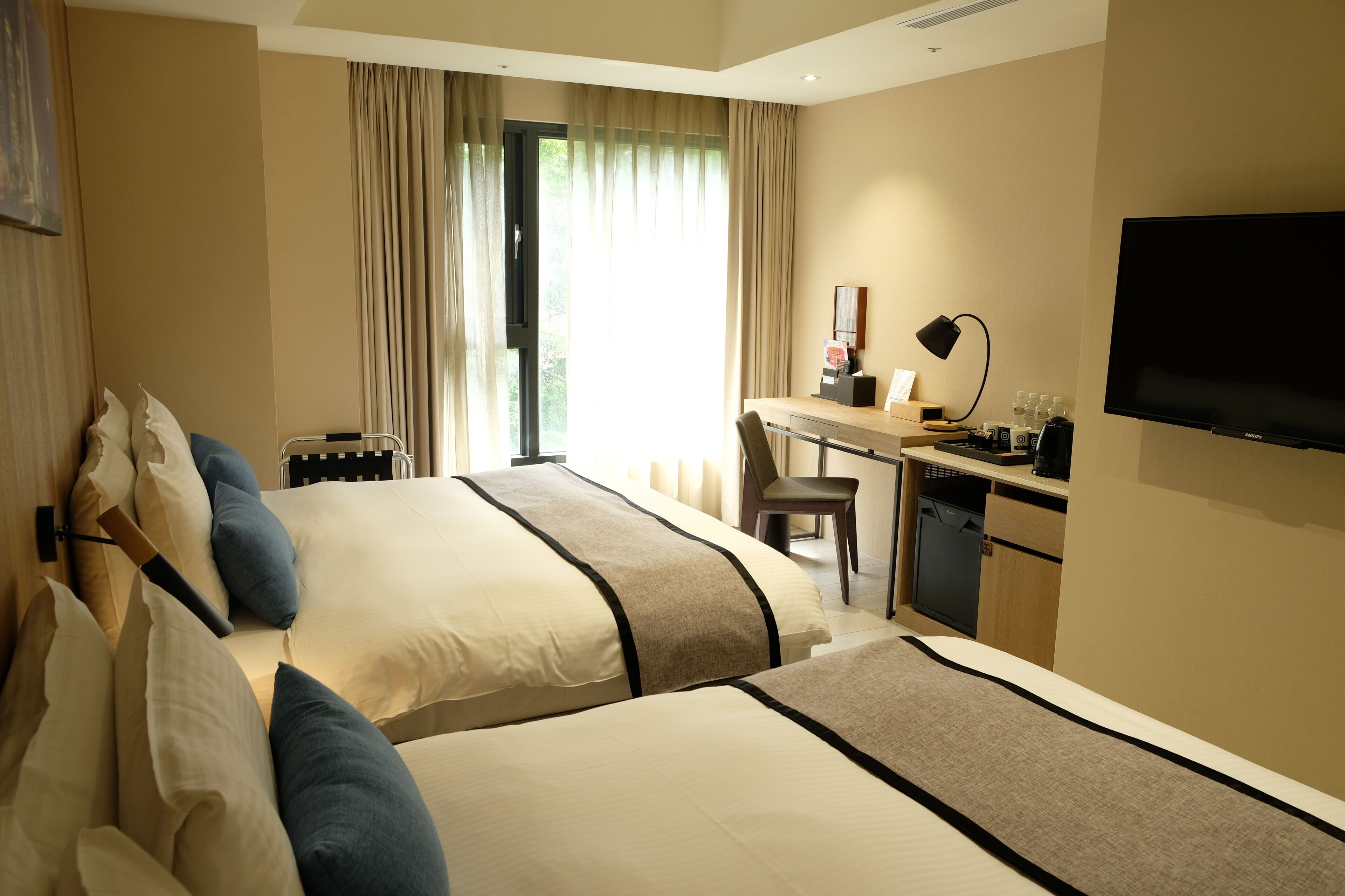 Ein Hotelzimmer mit zwei Betten, einem Schreibtisch, einem Sessel, einem Fernseher und einem Fenster mit Vorhängen.