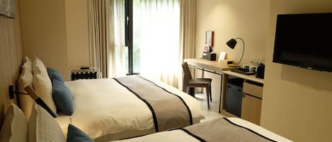 Ein Hotelzimmer mit zwei Betten, einem Schreibtisch, einem Sessel, einem Fernseher und einem Fenster mit Vorhängen.
