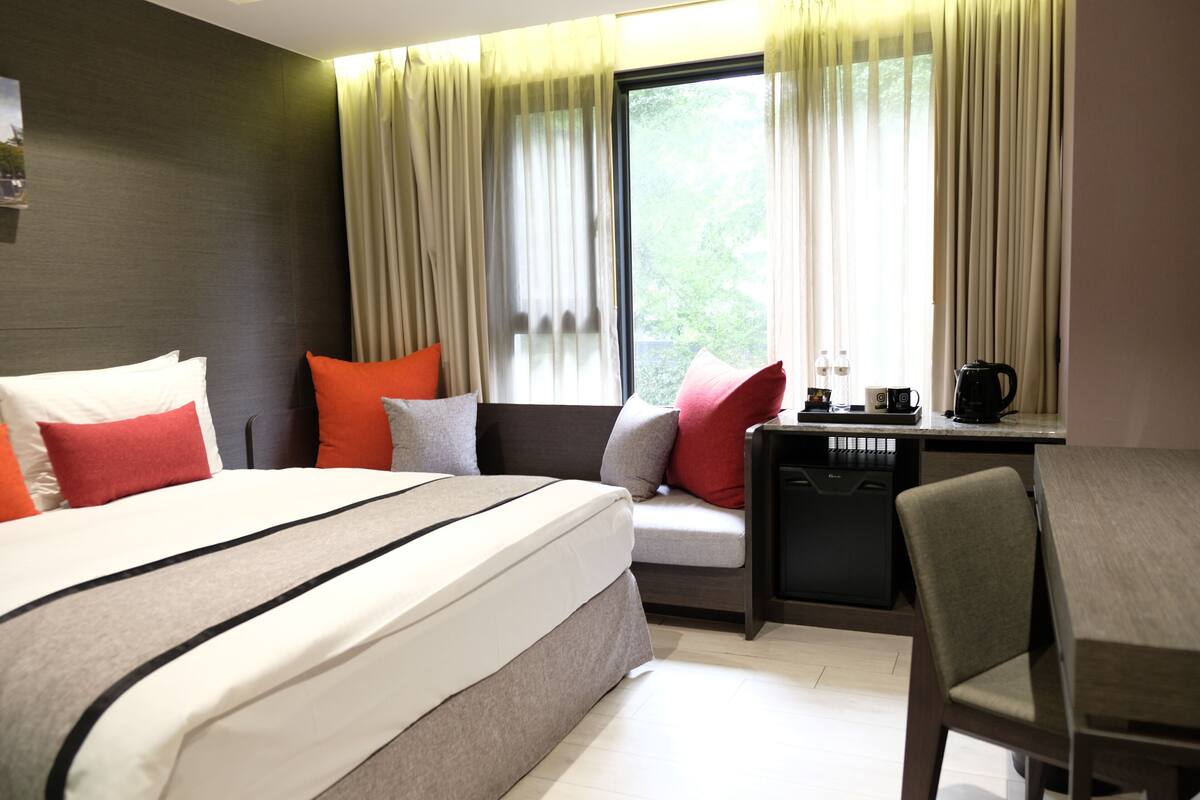 A hotel room with a bed, a desk, and a window with curtains.