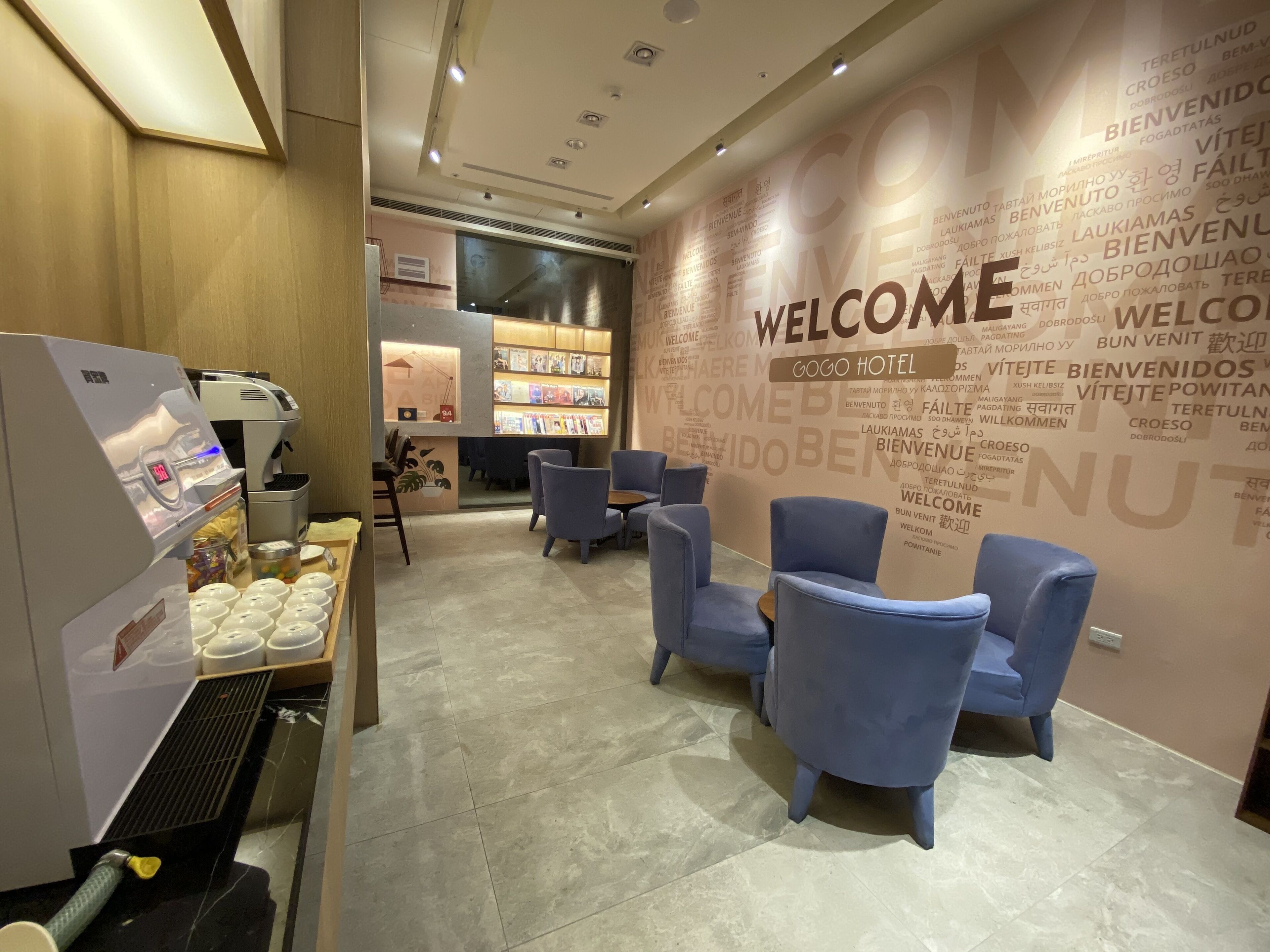 Un vestíbulo de hotel con un muro que dice 'WELCOME', zona de estar y una máquina de café.