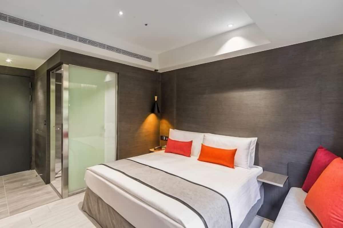 A modern hotel room with a large bed, a glass shower enclosure, and a small bedside table.