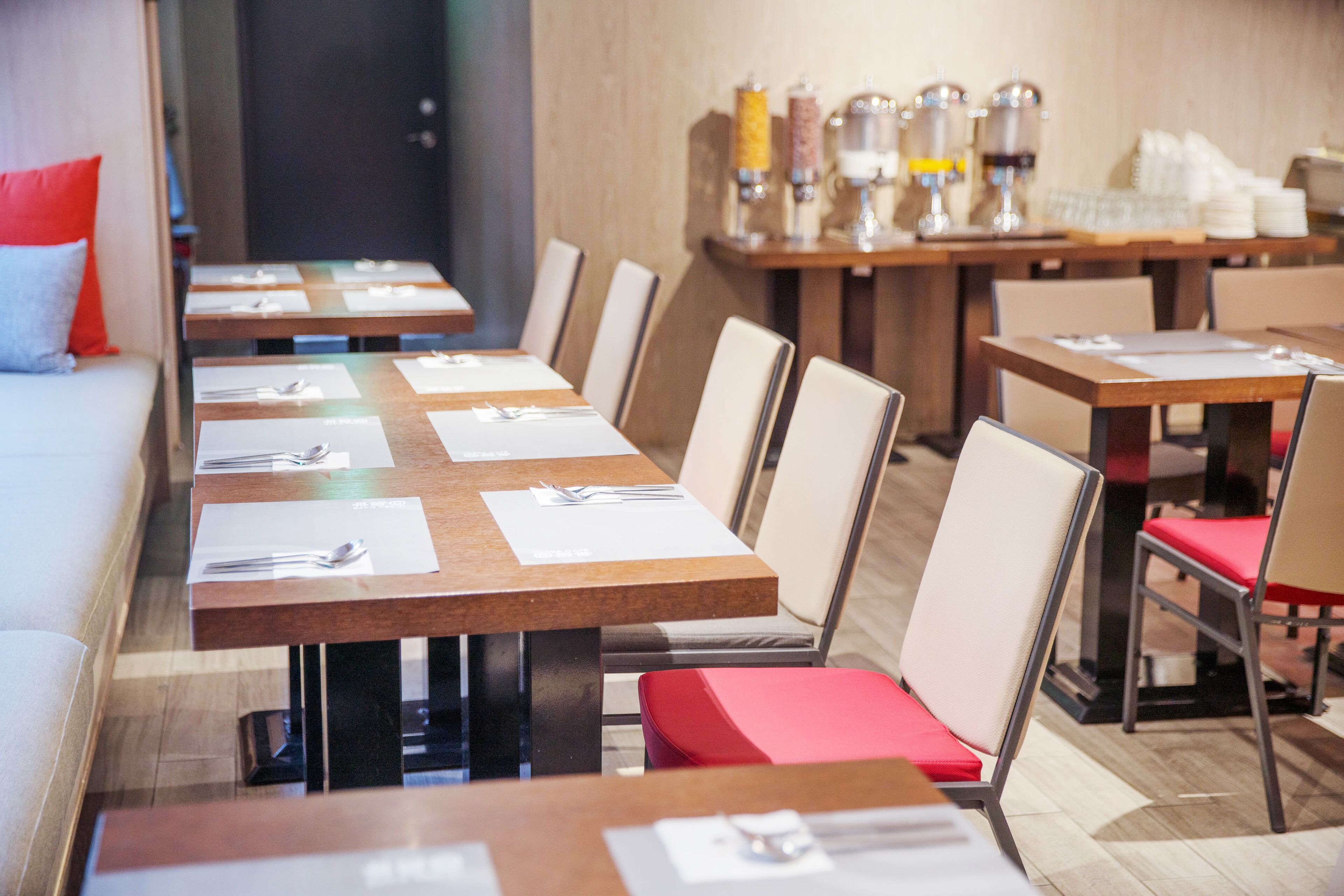 A restaurant with multiple tables and chairs, some with red cushions.