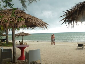 Una playa con sombrillas de techo de paja, una mesa roja y sillas.