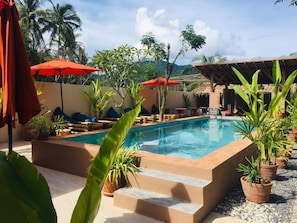 Una piscina al aire libre, sombrillas, sillones reclinables de piscina