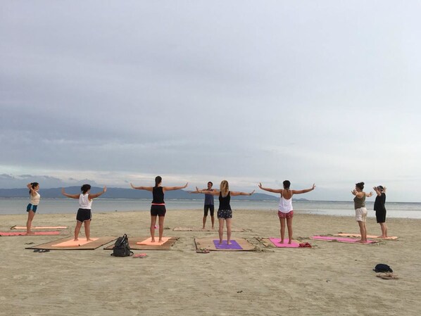 Un grupo de personas sobre tapetes de yoga en una playa bajo un cielo nublado.