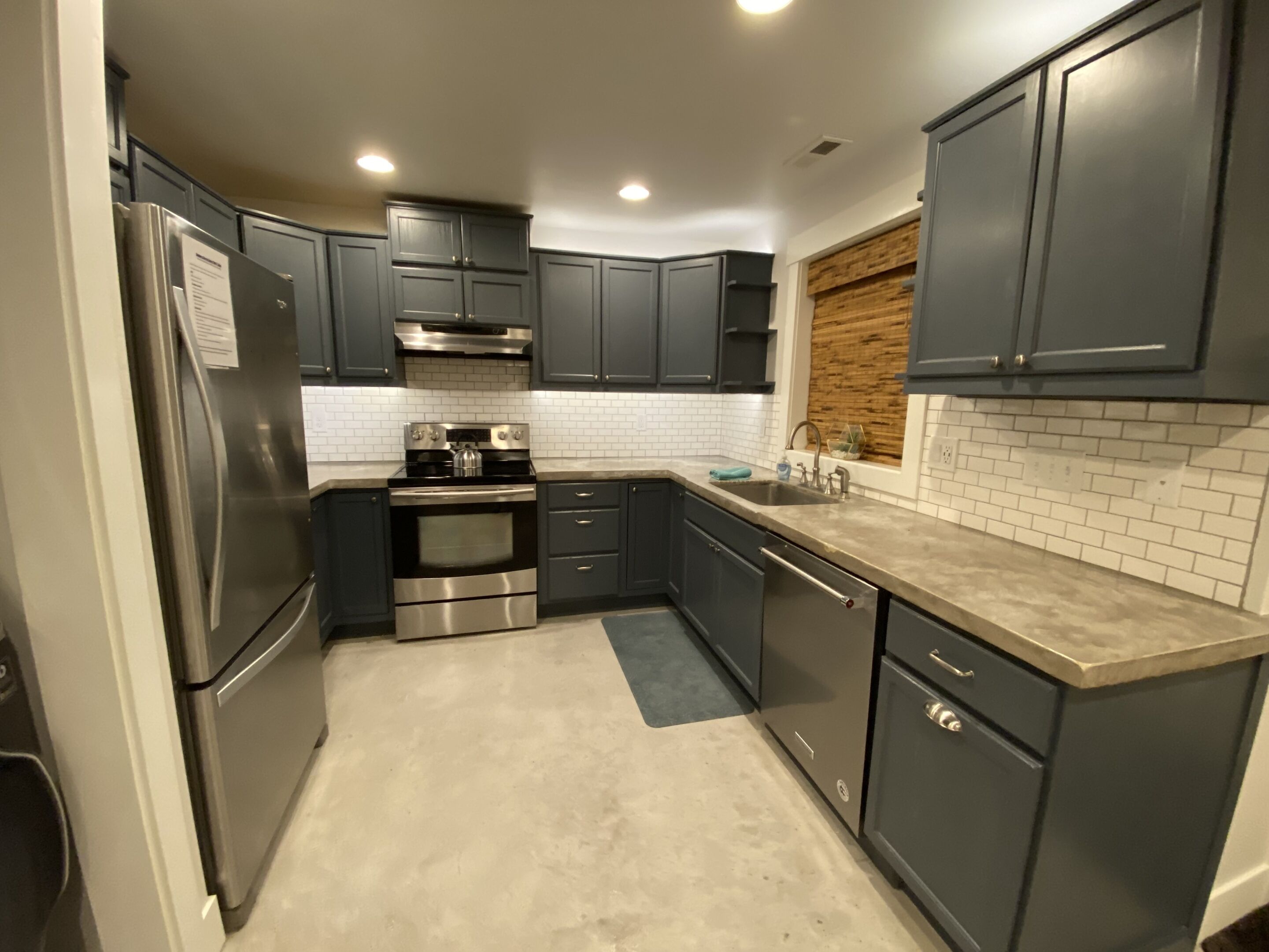 Una cocina compacta con armarios oscuros, electrodomésticos de acero inoxidable y un salpicadero de azulejos.