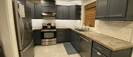 Una cocina compacta con armarios oscuros, electrodomésticos de acero inoxidable y un salpicadero de azulejos.