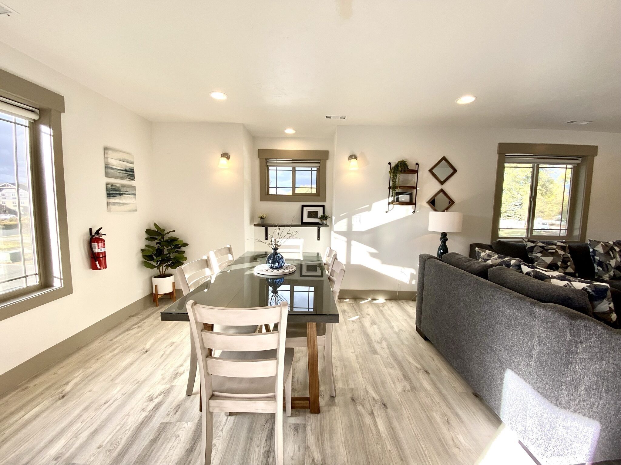 A modern living room with a grey sofa, a dining table with chairs, and a kitchen area in the background.