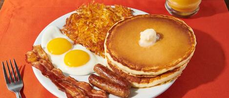 A breakfast plate with eggs, bacon, hash browns, pancakes, and a glass of orange juice.