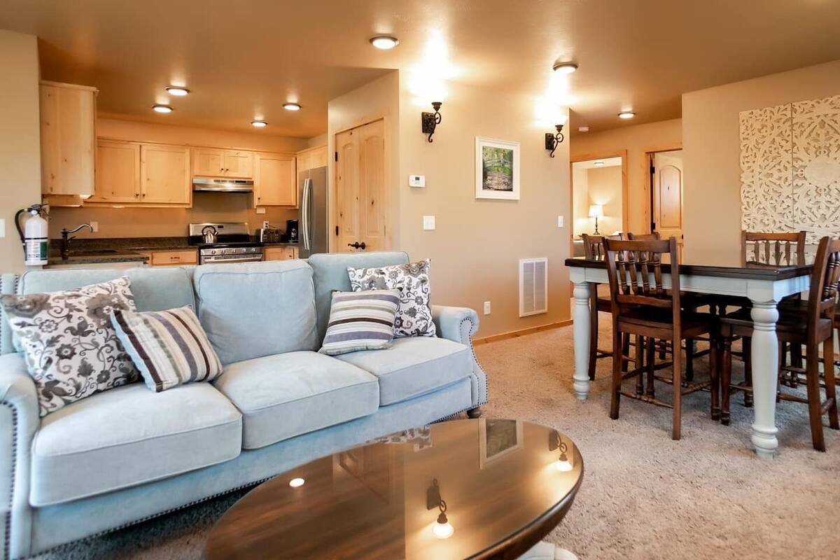 A modern living room with a light blue sofa, a wooden dining table with chairs, and a kitchen in the background.