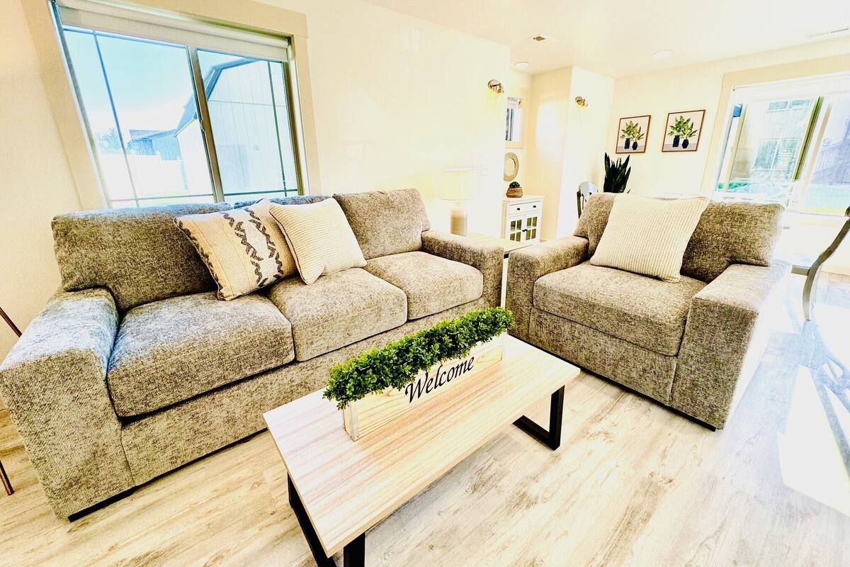 A living room with two sofas, a coffee table with a plant, and a 'Welcome' sign.