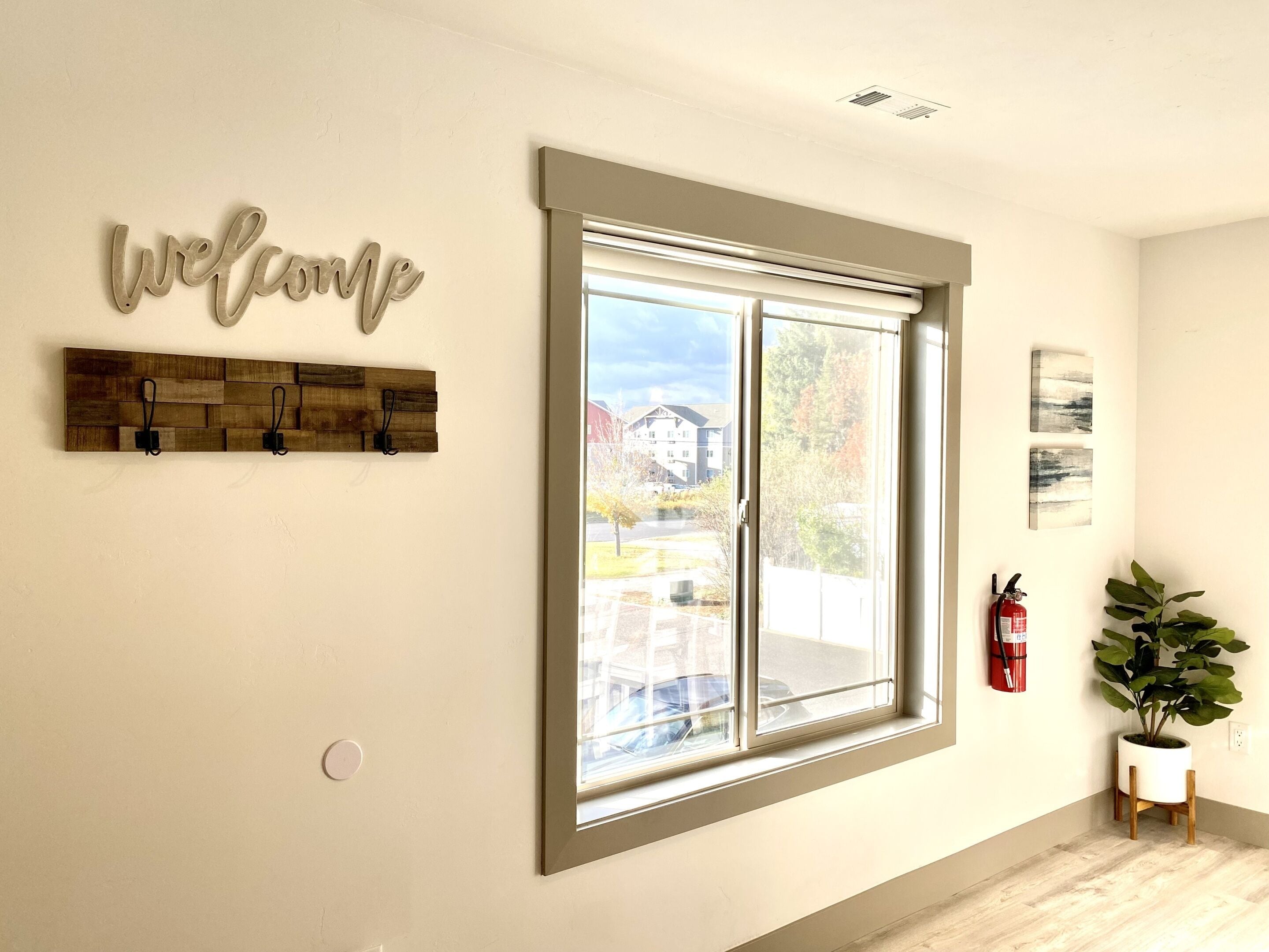 A room with a large window, a welcome sign, a fire extinguisher, and a potted plant.