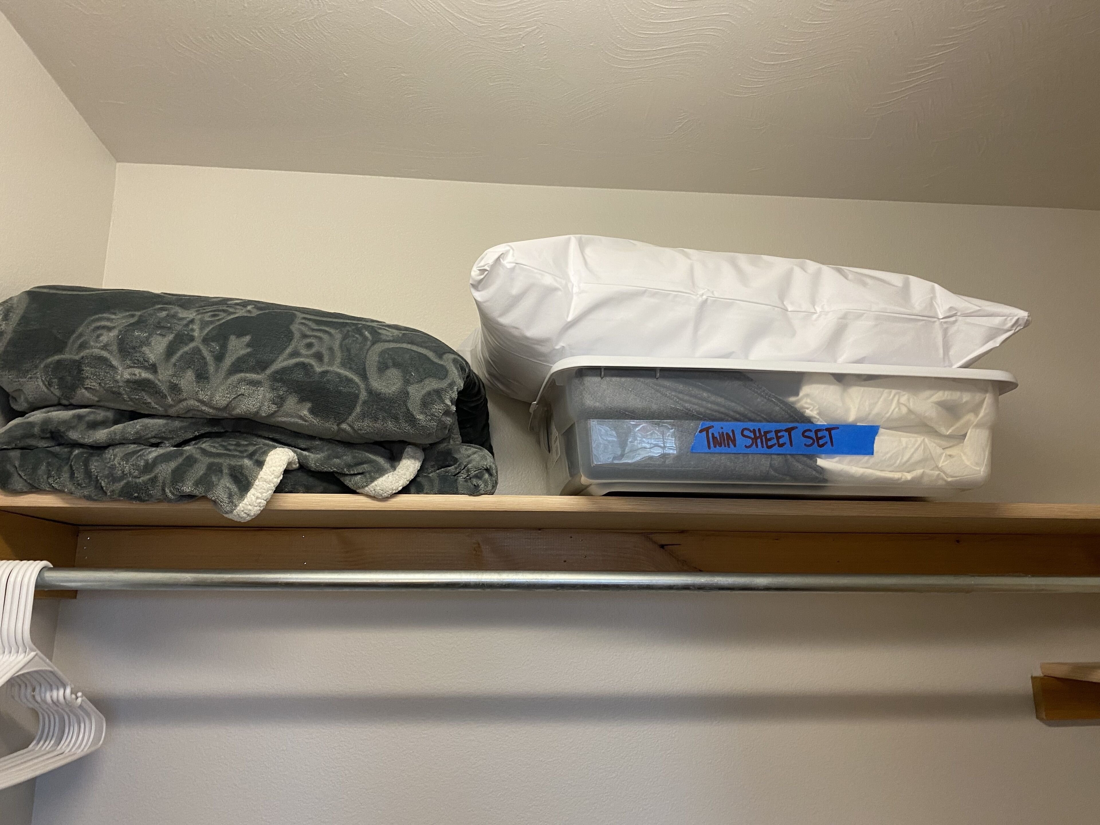 A storage shelf with a folded blanket and a labeled plastic container.