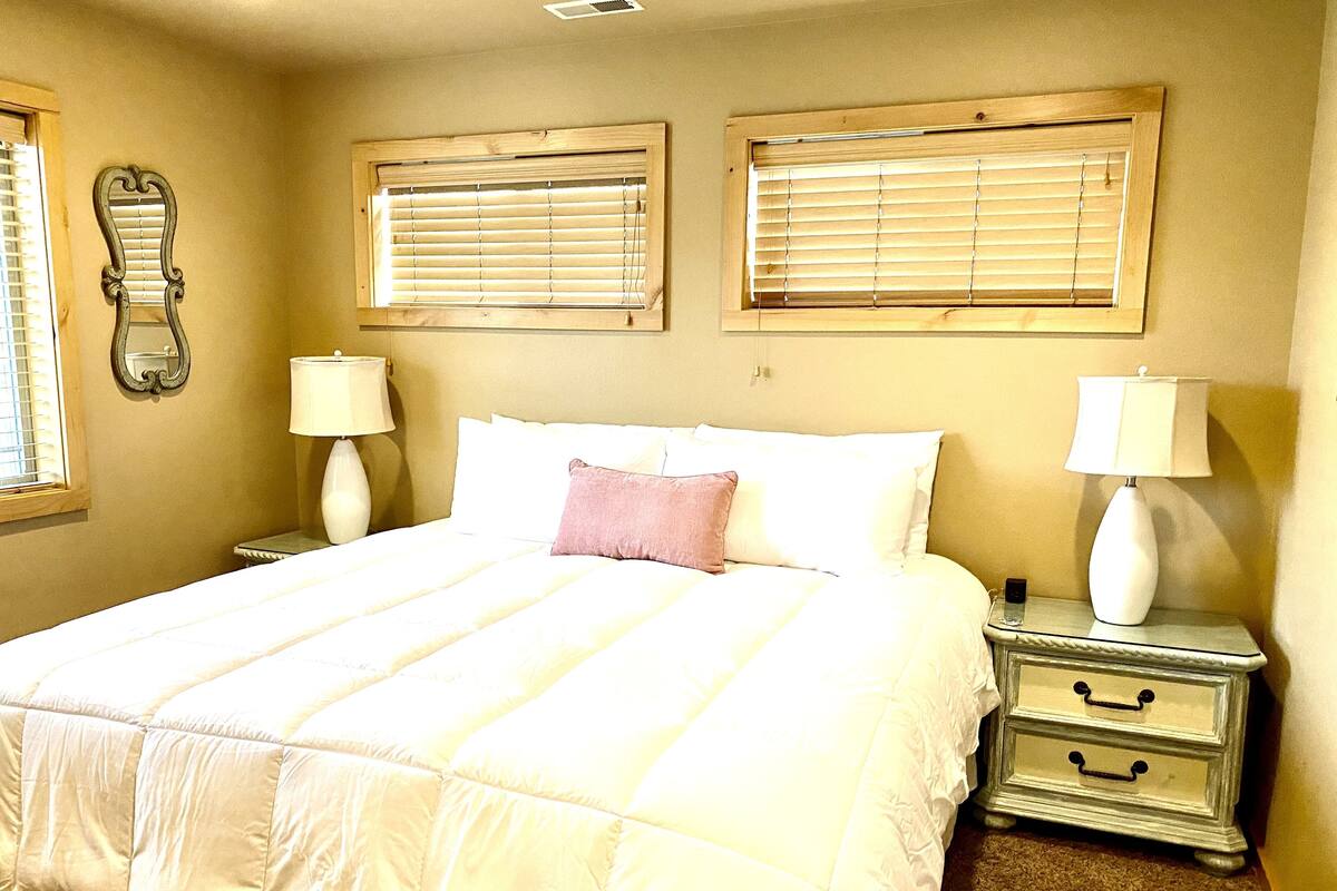 A neatly made bed with white bedding, two bedside lamps, and a nightstand with drawers.