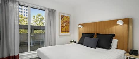 Ein Hotelzimmer mit einem großen Bett, einem Holzkopfende, einem Nachttisch mit Telefon und Blick ins Freie durch eine Schiebetür.