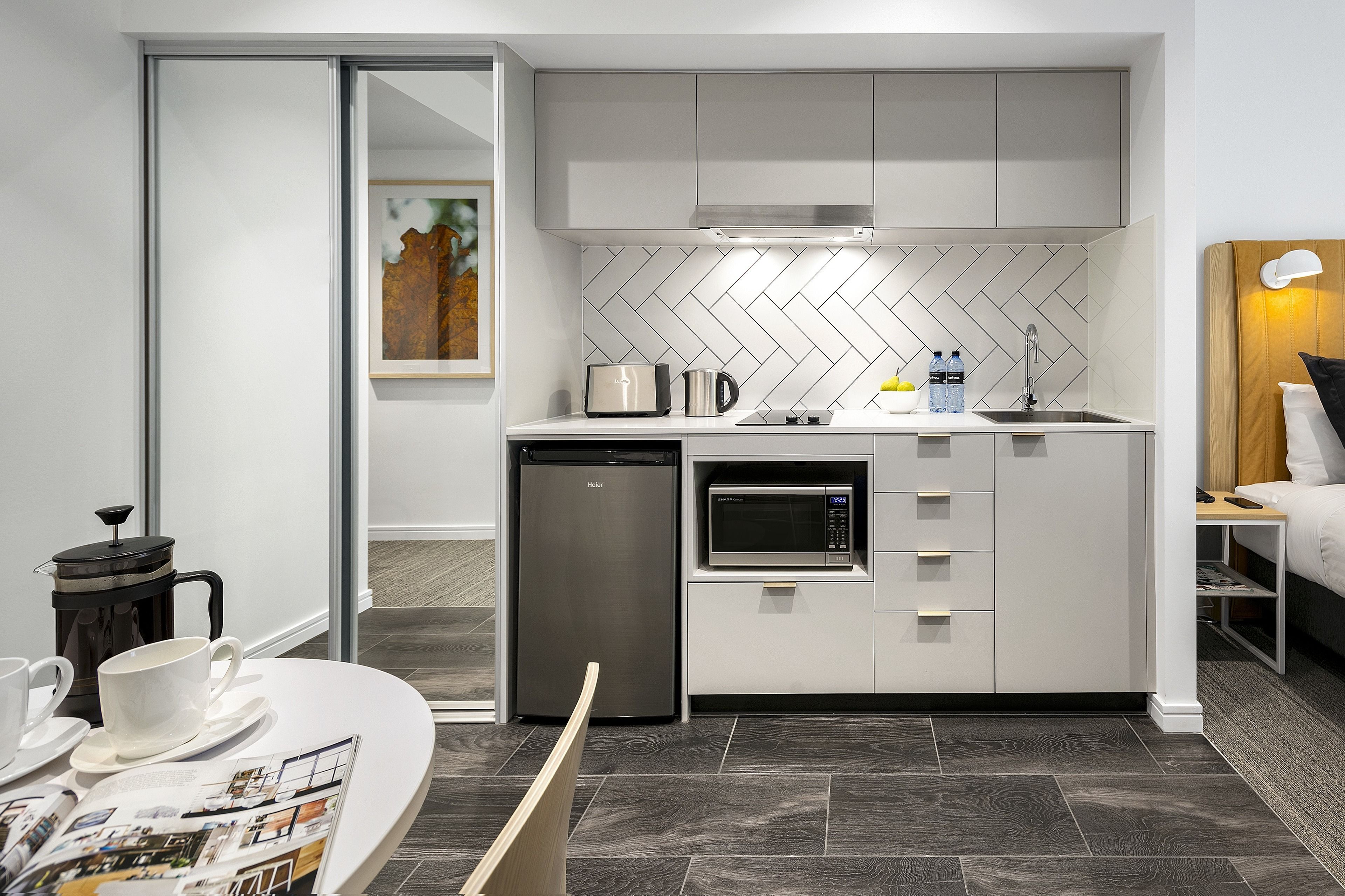 A compact kitchen with a microwave, toaster, and coffee maker, a dishwasher, and a herringbone-patterned backsplash.