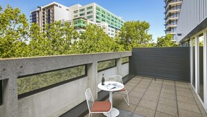 A balcony with two white chairs and a small round table, a concrete wall with a metal mesh design, and a view of modern buildings in the background. - Quest Canberra City Walk (Canberra)
